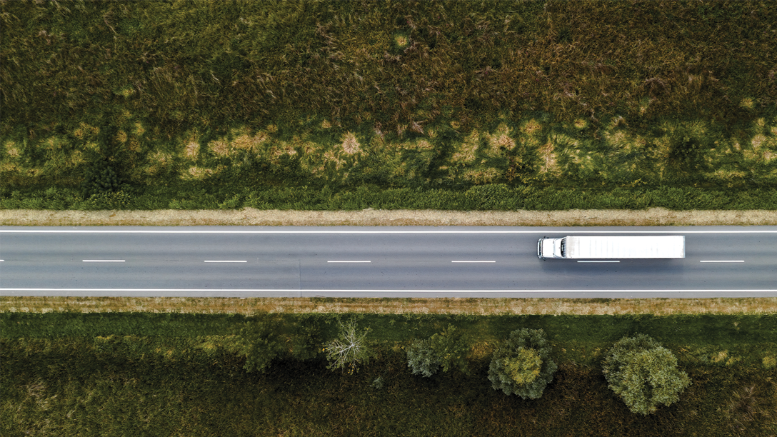 Tendencias y predicciones de Geotab para 2025 en la gestión de flotas. Vista aérea de un camión blanco circulando por una carretera rodeada de vegetación. La imagen evoca la importancia de la tecnología telemática en este sector en constante evolución.