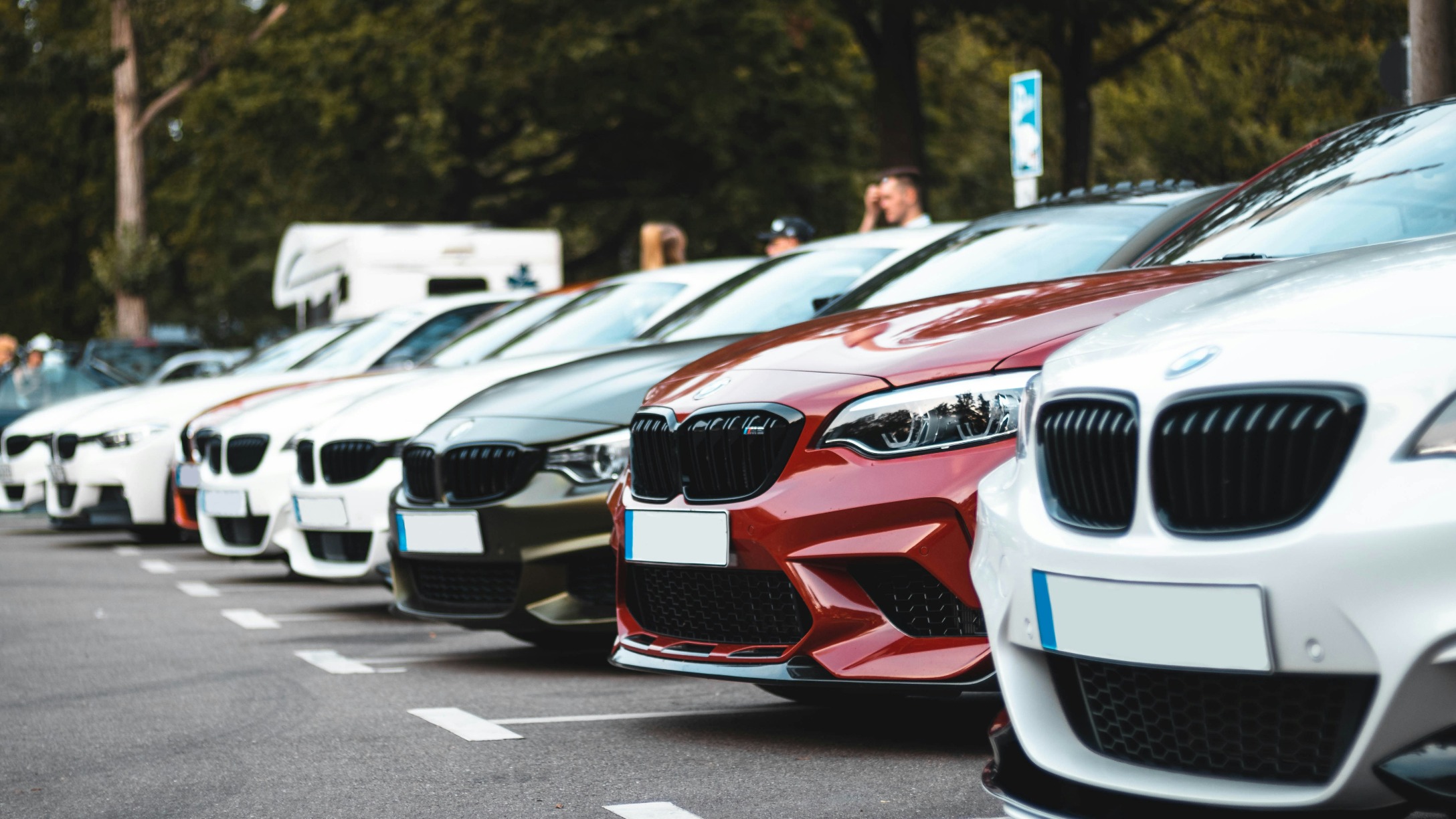 Serie di auto di diversi colori e marchi parcheggiate in un parcheggio e fotografate lateralmente.