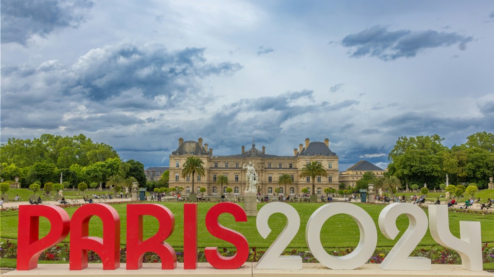 Scritta in bianco e rosso Paris 2024 e sullo sfondo un castello parigino