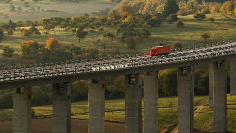 immagine di un veicolo rosso che attraversa un ponte in mezzo alla vegetazione