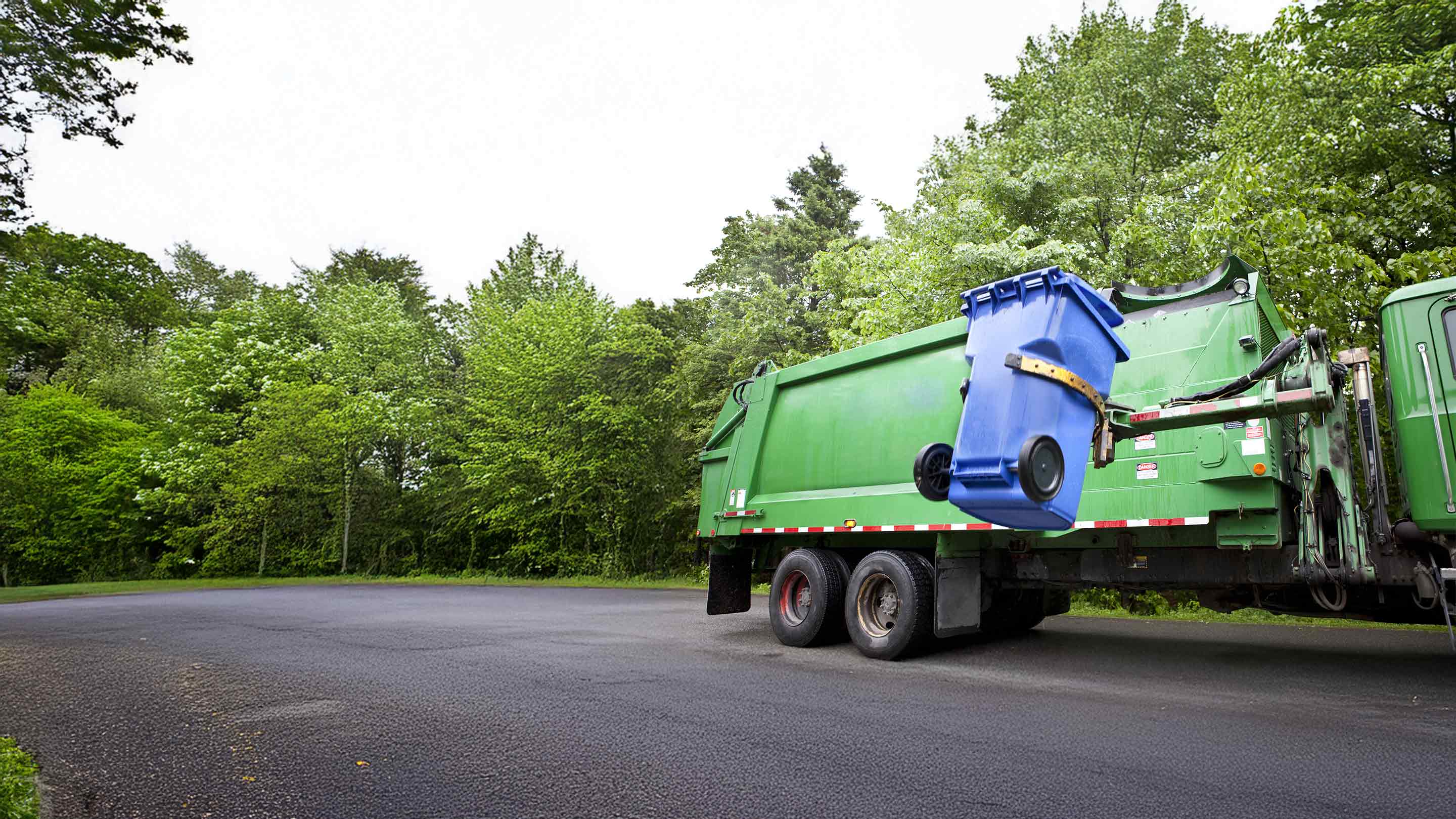 Green dump truck lifting a trash bin