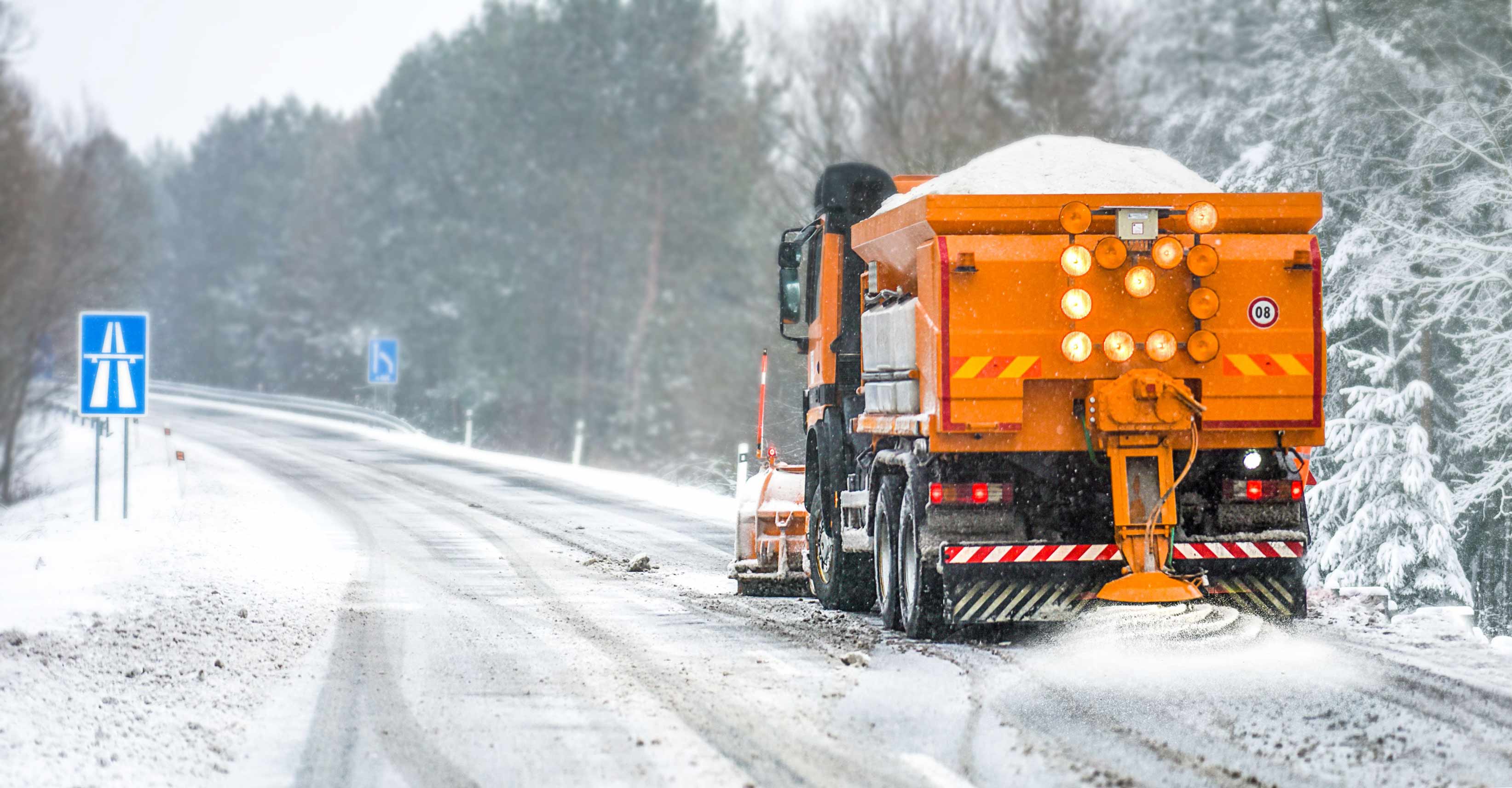 Orange snow plow driving down an empty road