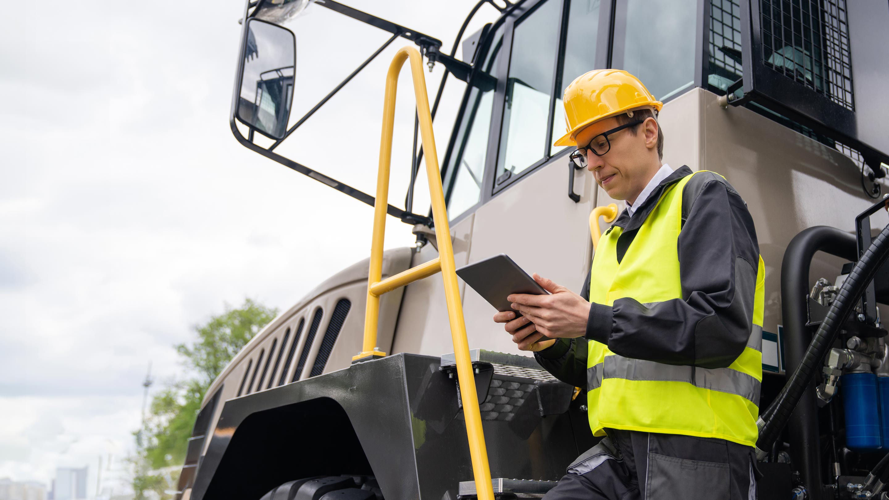 person standing next to a large construction truck using a tablet